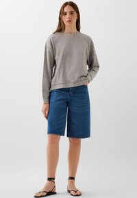 Sudadera gris con sutiles embellishments, combinada con pantalones cortos de mezclilla azul. El calzado consiste en sandalias planas negras con tiras.