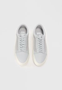 Adidașii gri deschis au partea superioară din piele texturată, design cu șireturi, tălpi de culoare crem și cusături decorative pe laturi.