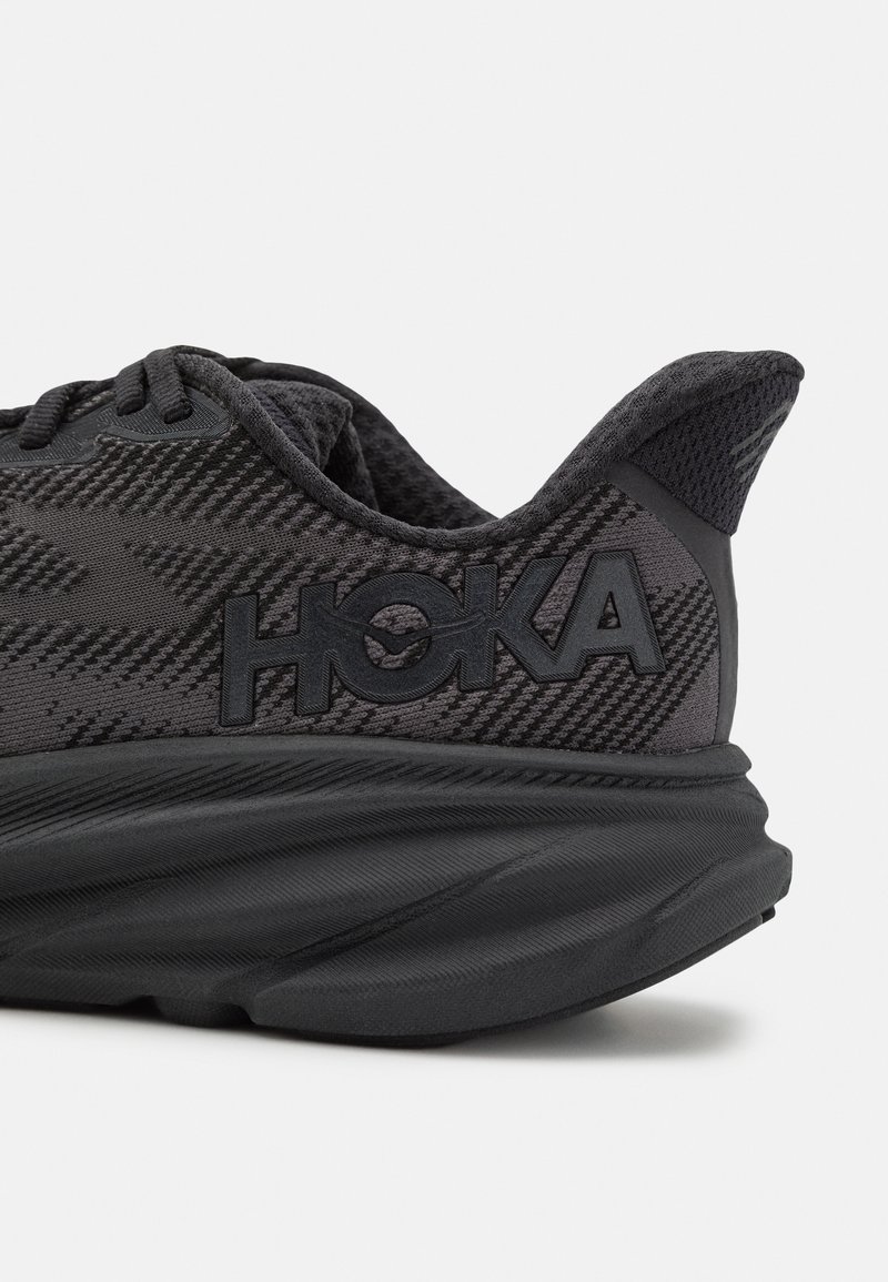 Schwarzer Sportschuh mit Mesh-Obermaterial, strukturiertem Muster, verstärkter Ferse und HOKA-Logo. Abgerundete Sohle mit sichtbarem Dämpfungsdetail.