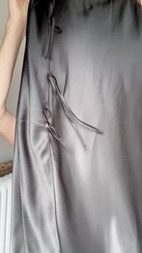 Händer som håller ett slätt, glänsande, mörkgrått satinfabric med tre knutna öglor på ena kanten.