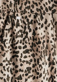 Tissu imprimé animal avec un fond beige et des taches brun foncé et noires. Texture douce avec un léger éclat ; comprend un petit détail d'étiquette.