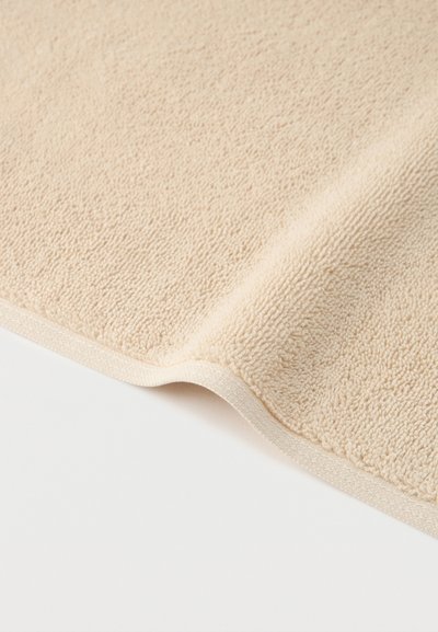 Υφασμα από απαλό μπεζ πετσέτα με υφή από θηλιές και τελειωμένη άκρη, σε λευκό φόντο.