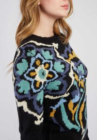 Pull en tricot noir avec un motif floral et géométrique multicolore, comportant des nuances de bleu, de vert et de jaune. Encolure ronde.