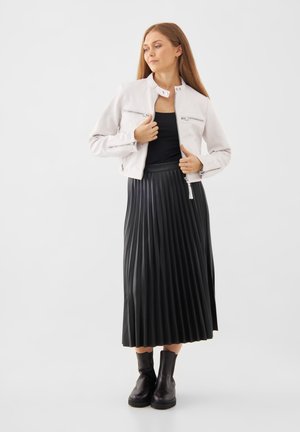 Chaqueta de cuero blanca con cremalleras, falda negra plisada y botines negros. La chaqueta tiene un cuello alto y bolsillos con cremalleras.