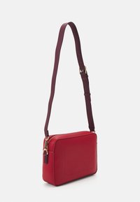 Czerwona skórzana torebka typu crossbody z zamknięciem na zamek, prostokątnym kszta�łtem, teksturowaną powierzchnią i regulowanym brązowym paskiem. Akcenty w kolorze złotym.