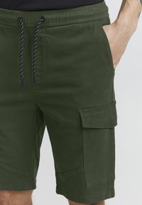 Cargo-Shorts aus einem olivgrünen Baumwollmix, mit einem elastischen Bund und schwarzem Kordelzug, Seitentaschen und gestickten Akzenten.