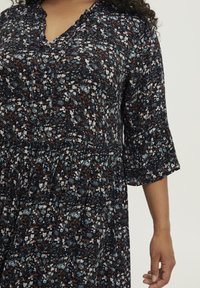 Kukkamekko, jossa on tummansininen tausta, lyhyet pöyheät hihat, pleated vyötärö ja sekoitus vaaleansinisiä, valkoisia ja ruskeita kuvioita.