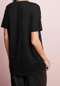 Sort bomulds t-shirt med korte ærmer, rund halsudskæring og slidser i siderne. Bagsiden har et enkelt design med en afslappet pasform.