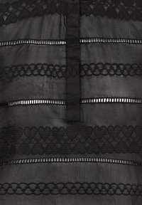 Svart textil med lager av horisontella ränder. Invecklad hjärtformad brodyr längs nederkanten, avbruten av smala utskärningar. Mjuk textur.