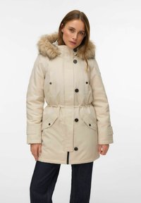 Bézs parka ar mākslīgās kažokādas kapuci, aizdari ar pogām un rāvējslēdzēju, elastīgu vidukli, divas priekšējās kabatas un ribotas aproces siltumam un komfortam.