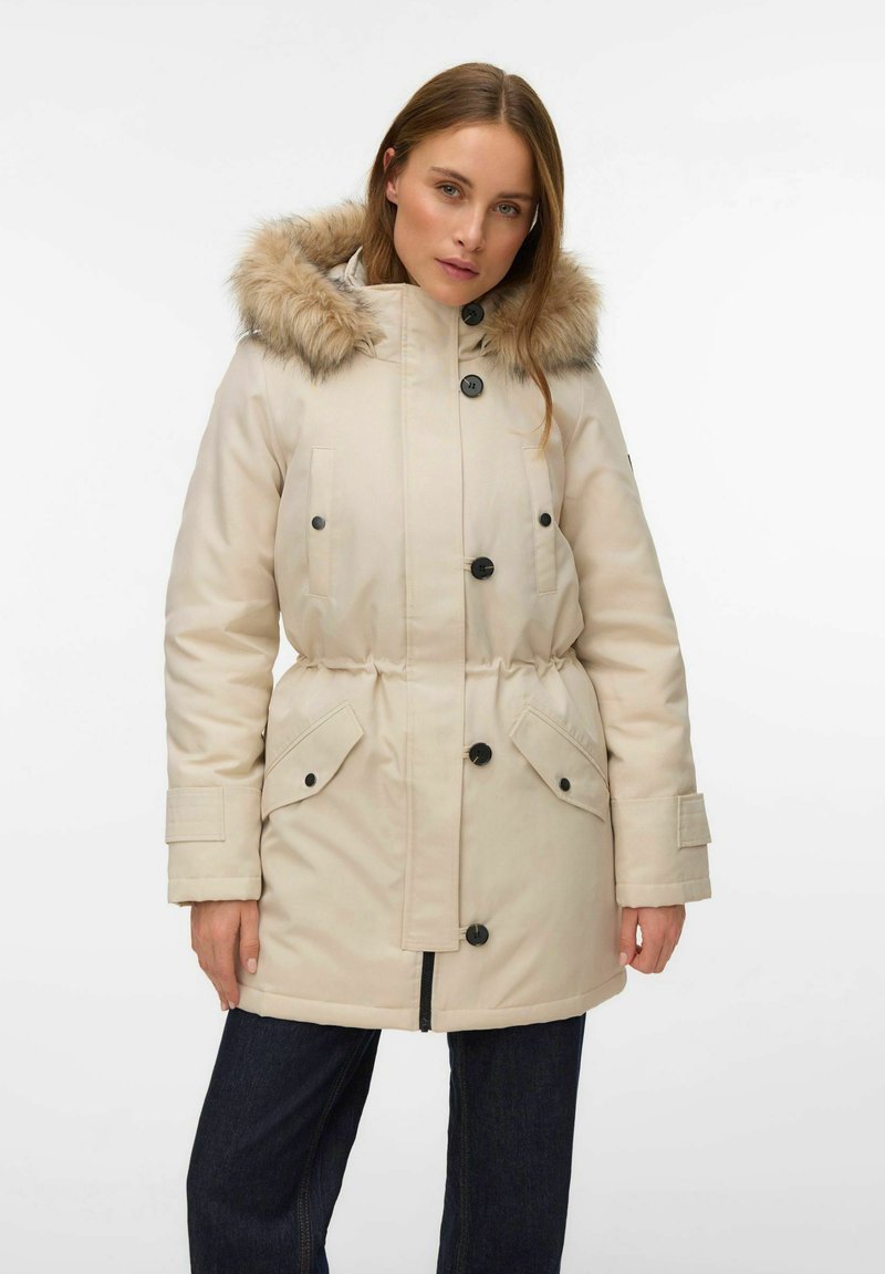 Bézs parka ar mākslīgās kažokādas kapuci, aizdari ar pogām un rāvējslēdzēju, elastīgu vidukli, divas priekšējās kabatas un ribotas aproces siltumam un komfortam.