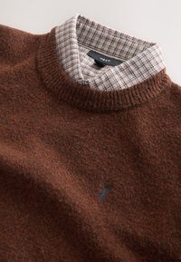 Brauner Wollpullover mit strukturierter Oberfläche, geripptem Halsausschnitt und einem karierten Hemdkragen in Grau und Rot mit einem kleinen Logodetail.