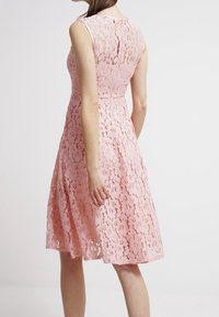 Krajkované šaty v jemné růžové barvě s přiléhavým živůtkem, rozšířenou sukní a bezramínkovým designem. Disponují složitými květinovými vzory a zipovým zapínáním na zádech.