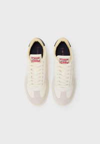 Lacoste tennis sneakers in cream with suede accents, featuring a lace-up closure, textured panels, and branding on the tongue.