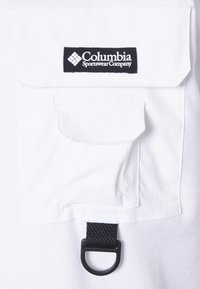 Camicia bianca con taschino sul petto con bottoni e un dettaglio a anello nero. Presenta una toppa con il logo "Columbia Sportswear Company" in bianco.