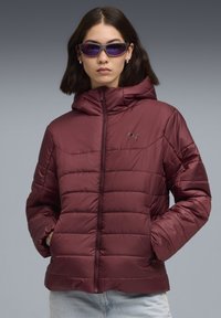 Bordeaux pufferjack met capuchon, geborduurd textuur en twee zijzakken. Voorzien van een rits aan de voorkant en een klein logo op de borst.