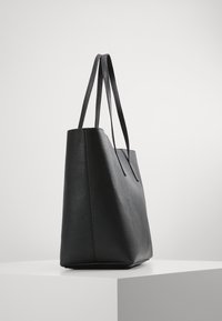 Sac fourre-tout en cuir noir avec une finition texturée, de forme rectangulaire haute et deux poignées. Design minimaliste sans quincaillerie visible.