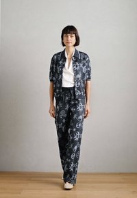 Ensemble assorti à motifs gris comprenant une chemise à col à manches courtes et un pantalon large, avec des accents blancs et une texture de tissu lisse.