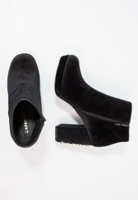 Botines de terciopelo negro con cremallera lateral, tacón cuadrado y acentos dorados con tachuelas en el tacón. Diseño elegante con una textura suave.