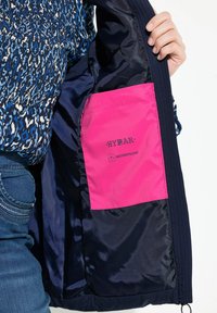 Marinblå vattentät jacka inuti med en rosa ficka märkt "HYRAR" och "WATERREPELLENT", med en slät, glansig yta.
