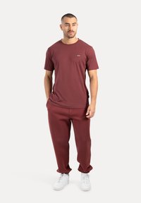 T-shirt in cotone bordeaux con maniche corte e scollatura tonda, abbinata a pantaloni della tuta in pile coordinati e sneakers bianche.