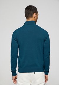 Teal pullovertröja med en falsk krage, ribbade ärmslut och nederkant. Tillverkad av ett mjukt material med en figurnära design för en ren silhuett.