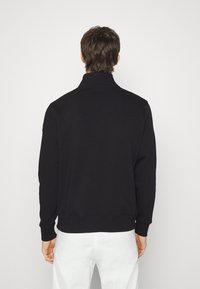 Svart zip-up sweatshirt med ståkrage, ribbade muddar och nederkant. Har en logo på vänster axel. Enkelt bakdesign.