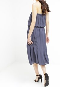 Axelbandslös, flödande midiklänning i mörkblått tyg med elastisk midjeresår. Klänningen har en avslappnad silhuett och mjuk drapering.