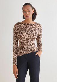 Langærmet top i leopardmønster i brune og sorte farver lavet af blødt, strækbart stof, parret med mørke bukser. Lige pasform og rund halsudskæring.