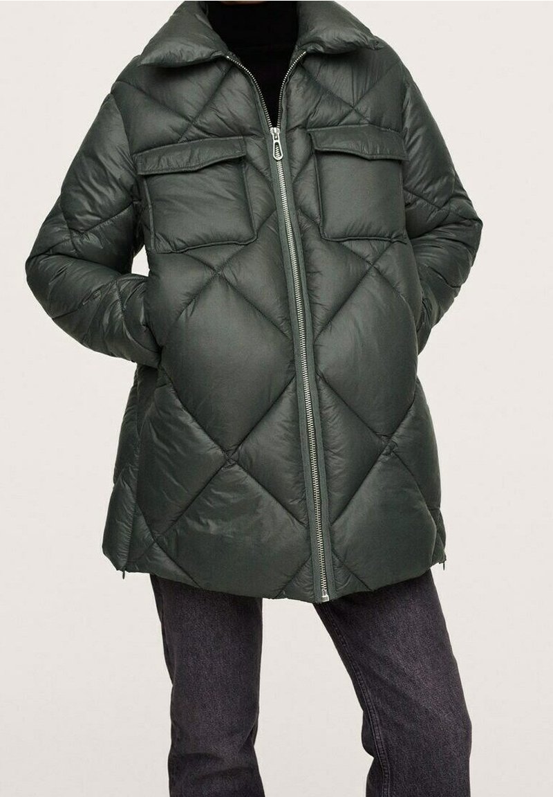 Veste matelassée vert foncé avec fermeture éclair à l'avant, deux poches poitrine et poches latérales, portée avec un pantalon foncé.