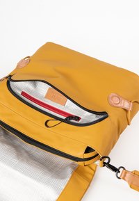 Borsa in pelle gialla con apertura a zip, dotata di una fodera a quadri grigia, una tasca interna rossa e dettagli in pelle marrone.