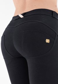 Sorte leggings i strækstof med tætsiddende design, baglommer og en lille guldfarvet logo-accent nær taljebåndet.