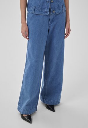 Szerokie niebieskie jeansy z dżinsu połączone z czarnymi butami w szpic, noszone z dopasowaną niebieską kurtką z dżinsu.