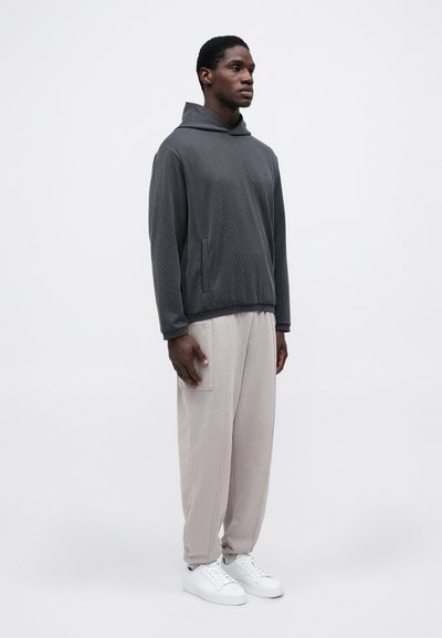 Grå hettegenser med teksturert design, kombinert med lyse beige joggebukser med sidelommer, og hvite sneakers.