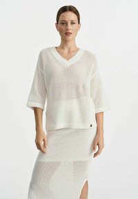 Biały dzianinowy top z dekoltem w kształcie V i luźnymi krótkimi rękawami, zestawiony z pasującą siateczkową spódnicą z bocznym rozcięciem i prążkowanym wykończeniem.