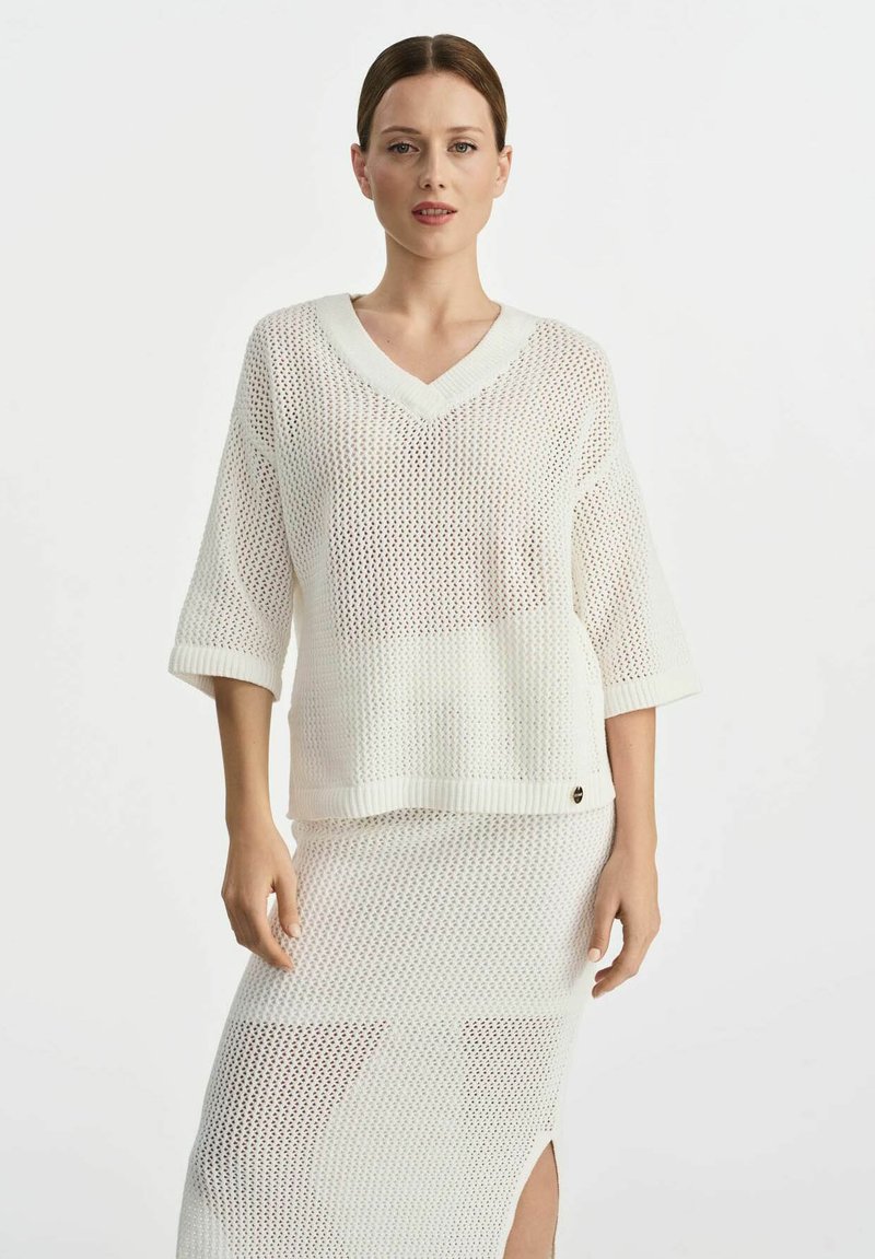 Biały dzianinowy top z dekoltem w kształcie V i luźnymi krótkimi rękawami, zestawiony z pasującą siateczkową spódnicą z bocznym rozcięciem i prążkowanym wykończeniem.