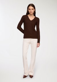 Maglione a V a coste marrone abbinato a pantaloni a gamba larga color crema chiaro e décolleté a punta marroni. Texture liscia con design lavorato a maglia.