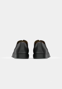 Black leather shoes with a smooth finish, slight heel, rounded toe, and a minimalist design. Exposed stitching details at the back.