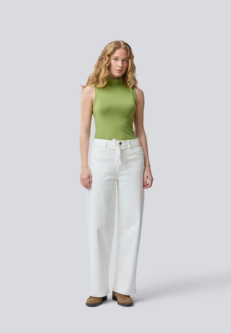 Top sin mangas verde con un escote alto, combinado con pantalones de pierna ancha blancos de cintura alta, que presentan una cintura atada y calzado marrón.