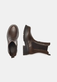 Bottines en cuir marron avec des panneaux élastiques sur les côtés, bout arrondi, semelle plate en caoutchouc et tirant pour un enfilage facile. Texture lisse avec un minimum de détails.