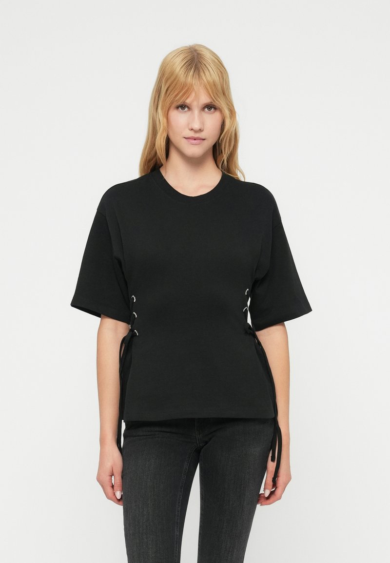 Μαύρο κοντομάνικο t-shirt με άνετη εφαρμογή, με κορδόνια στα πλαϊνά με μεταλλικά κουμπώματα, κατασκευασμένο από λείο ύφασμα.
