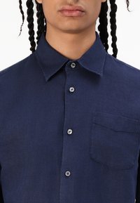 Camicia a maniche corte blu navy realizzata in tessuto testurizzato, caratterizzata da un colletto con bottoni, due bottoni e una tasca sul petto.