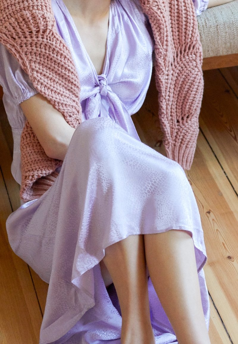 Lila satin klänning med ett knyt vid midjan, med ett mönster av ormskinn. Lager på lager med en korallfärgad stickad kavaj som visar texturdetaljer.