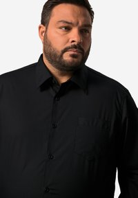 Černá košile na knoflíky s límečkem, přední kapsou a hladkou texturou látky. Navržena v klasickém střihu s jemným leskem.