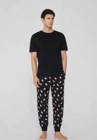 Camiseta de algodón negra combinada con pantalones de pijama negros que presentan un diseño de palomitas rojas sobre un fondo negro. Ajuste casual y puños en los tobillos.