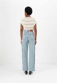 Ievīlota adīta blūze ar īsām piedurknēm krēmkrāsā, apvienota ar augsta jostasvietas gaiši ziliem platām kājām džinsiem, kuriem ir sānu šuves un gaišu kambariņu ādas etiķete.