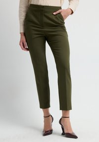 Grüne, taillierte Hosen mit hoher Taille, Vorderfalten und glatter Textur. Kombination mit burgunderfarbenen, spitzen Absätzen mit Knöchelriemen.