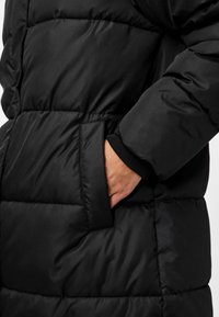 Casaco acolchoado preto com design em matelassê, apresentando um bolso lateral, punhos canelados e uma textura suave.