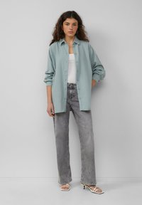 Camisa de botones azul claro con una tela texturizada, combinada con jeans grises de cintura alta y tacones blancos con tiras.
