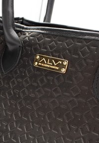 Czarna torebka teksturowana z geometrycznym wzorem, z złotą plakietką z logo i czarnymi skórzanymi uchwytami.